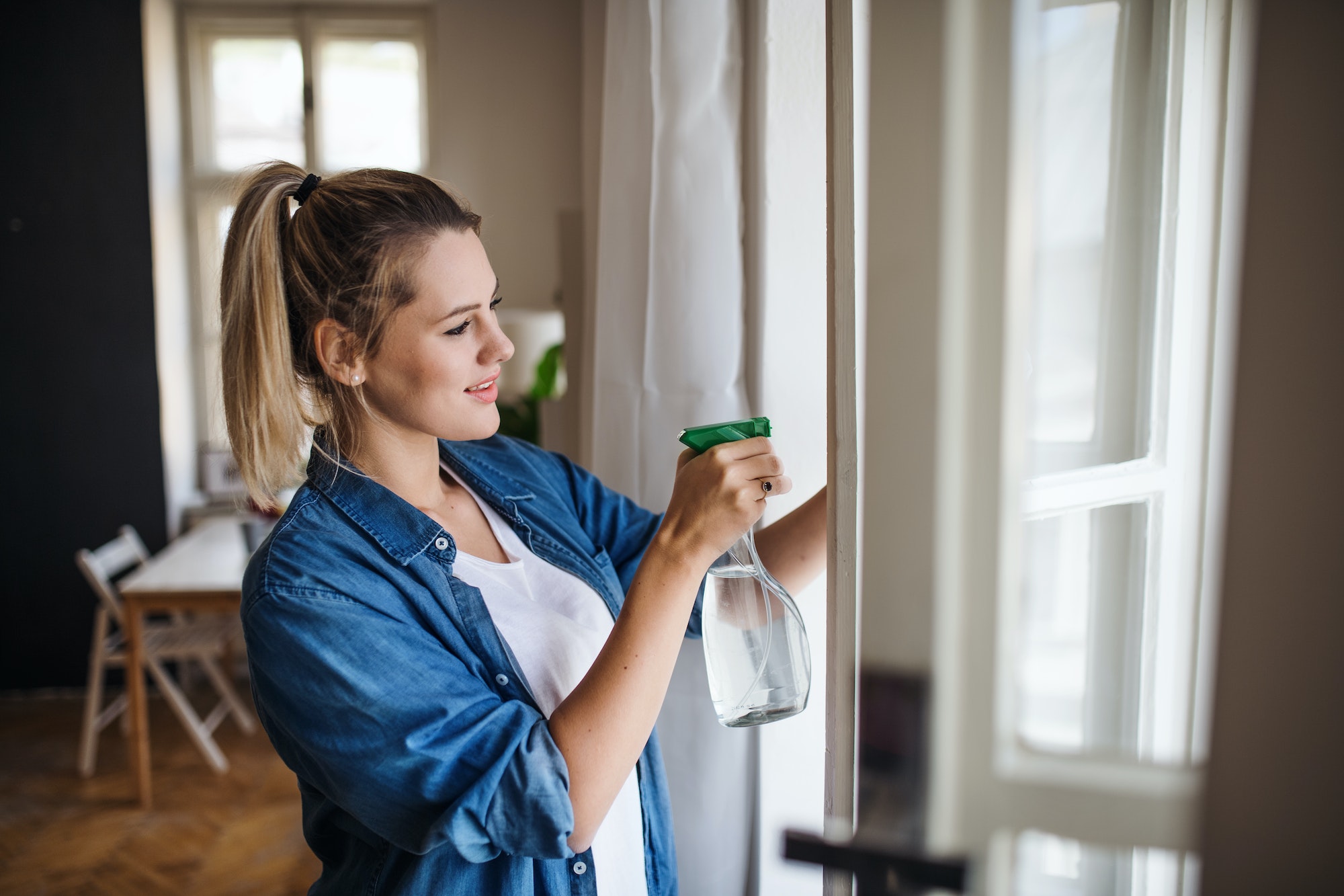 Young woman standing indoors at home, cleaning windows.